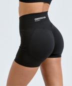 Black high-waisted compression shorts with a white 'OBSIDIAN PADEL' logo on the waistband, shown on a model from a rear three-quarter angle against a light gray background.