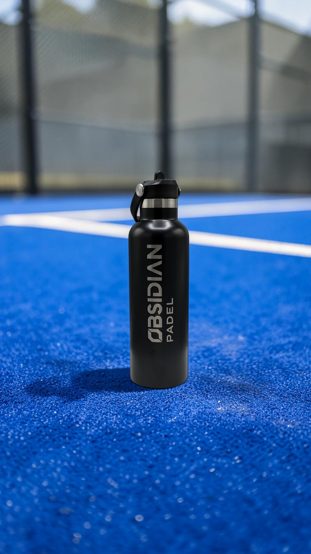 Obsidian Padel matte black insulated water bottle with integrated cage clip standing on a blue padel court.